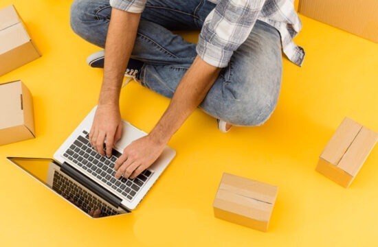 homem-de-calca-jeans-sentado-no-chao-utiliza-notebook-em-fundo-laranja-pesquisando-sobre-ecommerce-brasileiro