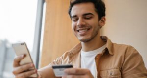 Homem sorridente segurando um celular e um cartão