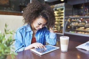 mulher sorrindo enquanto mexe no tablet em uma cafeteria