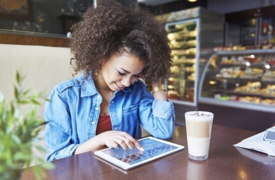 mulher sorrindo enquanto mexe no tablet em uma cafeteria