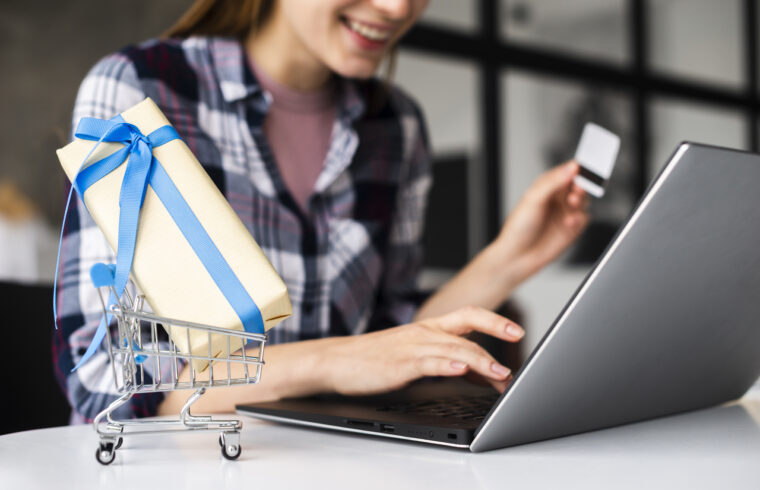 mulher fazendo compras online no seu computador enquanto segura um cartão de crédito em sua mão