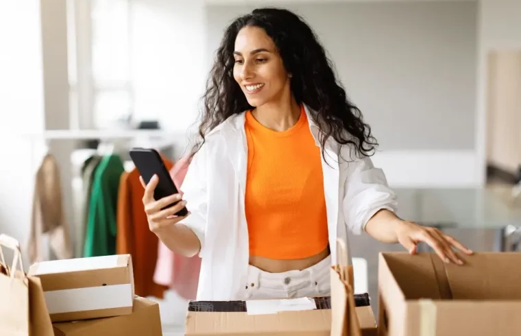 mulher-com-caixas-de-embalagem-segurando-smartphone-gerenciando-pedidos-de-roupas