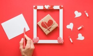 mão-proxima-de-um-papel-em-uma-mesa-decorada-com-moldura-de-coraçao