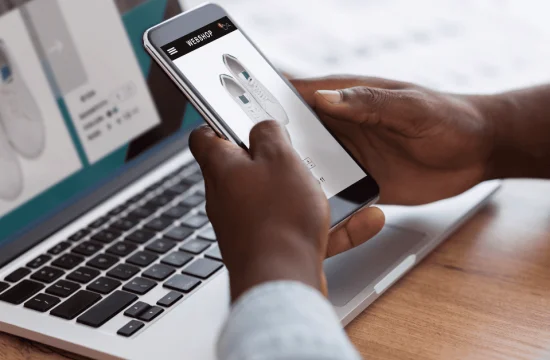 Homem-negro-fazendo-compras-on-line-com-smartphone-e-laptop-em-ambientes-fechados