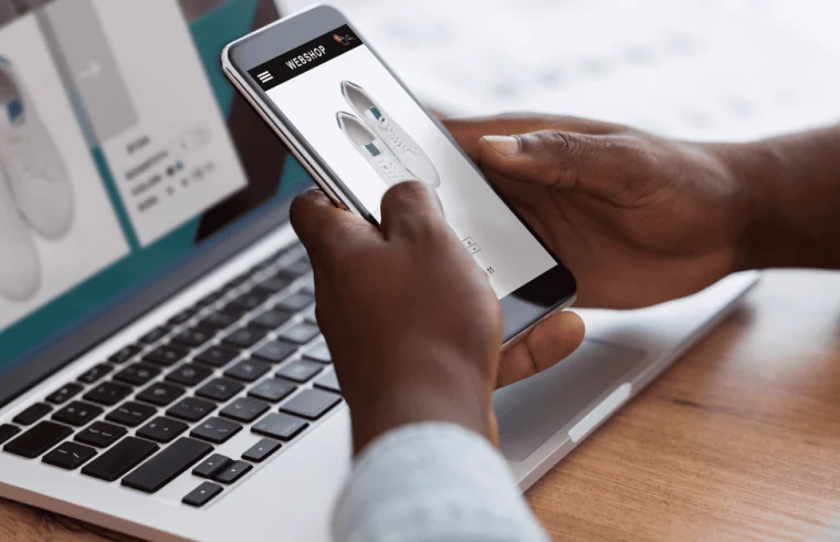 Homem-negro-fazendo-compras-on-line-com-smartphone-e-laptop-em-ambientes-fechados